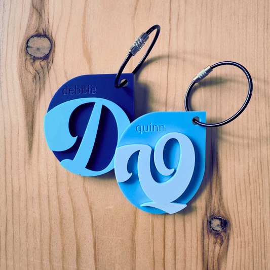 Blue and navy keychains with personalized names on a wooden surface