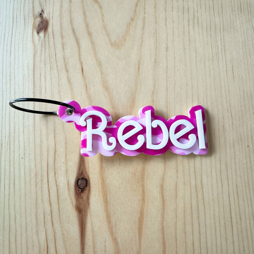 Keychain with a pink camouflage background and single colored name overlaid in acrylic with a wire keyring