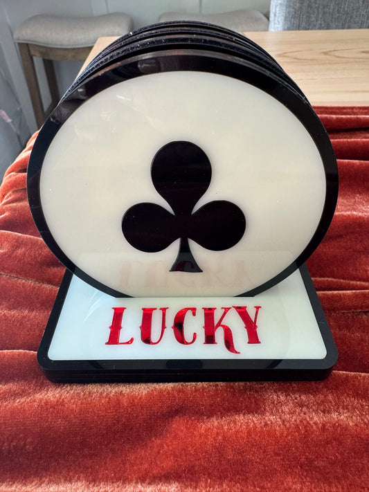 Decorative item with a black clover symbol and 'LUCKY' text on a white background, placed on a red surface.