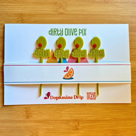 Product packaging for dirty olive cocktail picks with colorful characters and 'Dopamine Drip' branding on a wooden surface