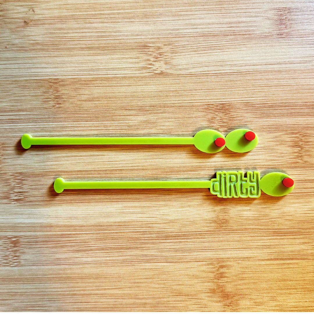 Two olive themed swizzle sticks with the word dirty etched in one.