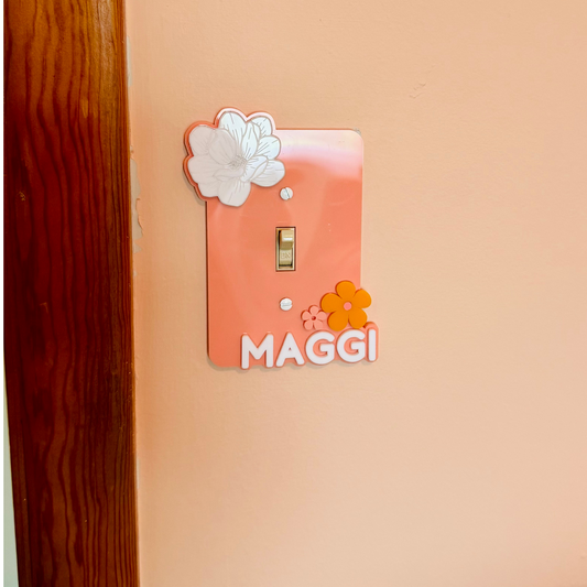 Decorative acrylic light switch cover with flowers and name text on a peach background.