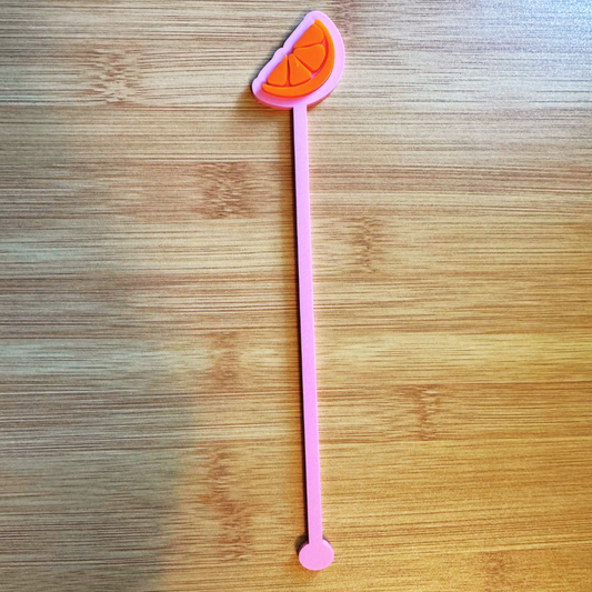 Pink stirrer with orange slice end on a wooden surface