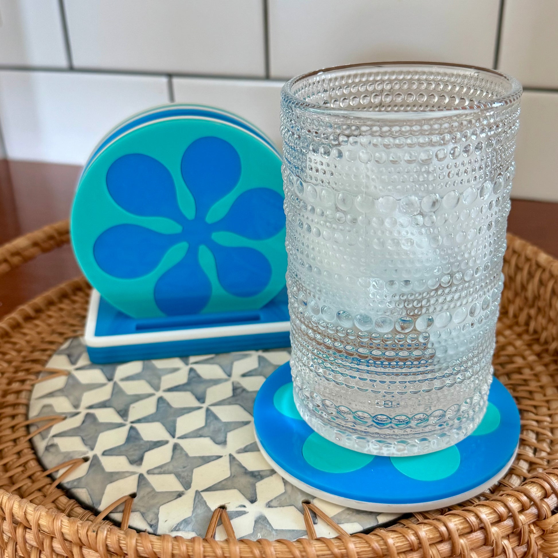 Clear glass on a blue coaster with a retro flower patterned coaster underneath, all on a woven tray.