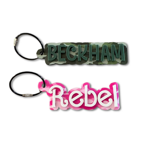 two keychains with a camouflage background and single colored name overlaid in acrylic with a wire keyring