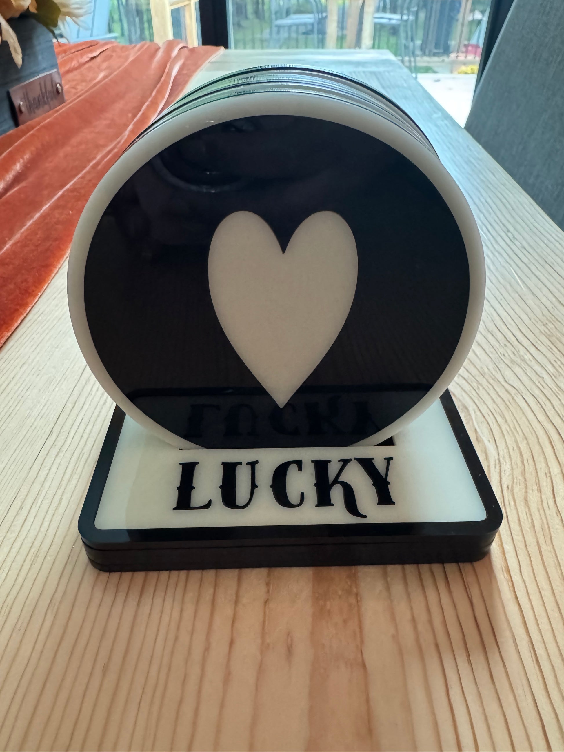 Round black coaster with a white heart and 'LUCKY' text in a coaster holder.