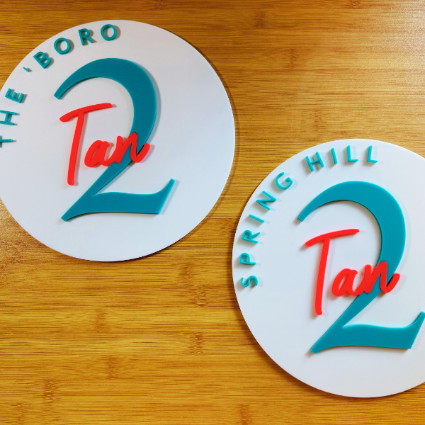 Two circular signs with 'Tan 2' branding on a wooden surface