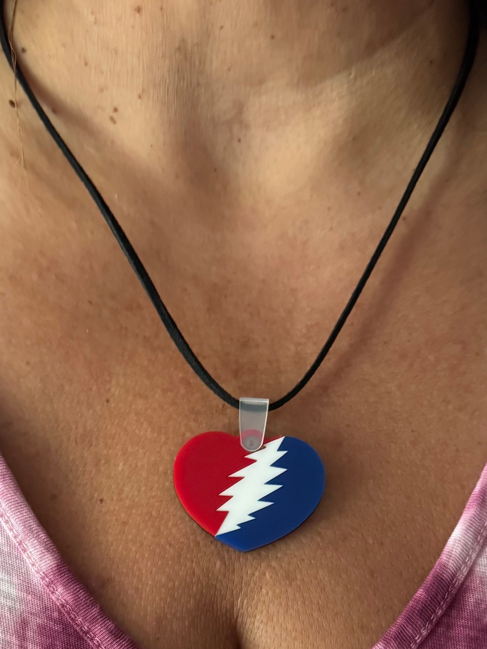 Heart-shaped pendant with red and blue design on a black cord, worn by a person.