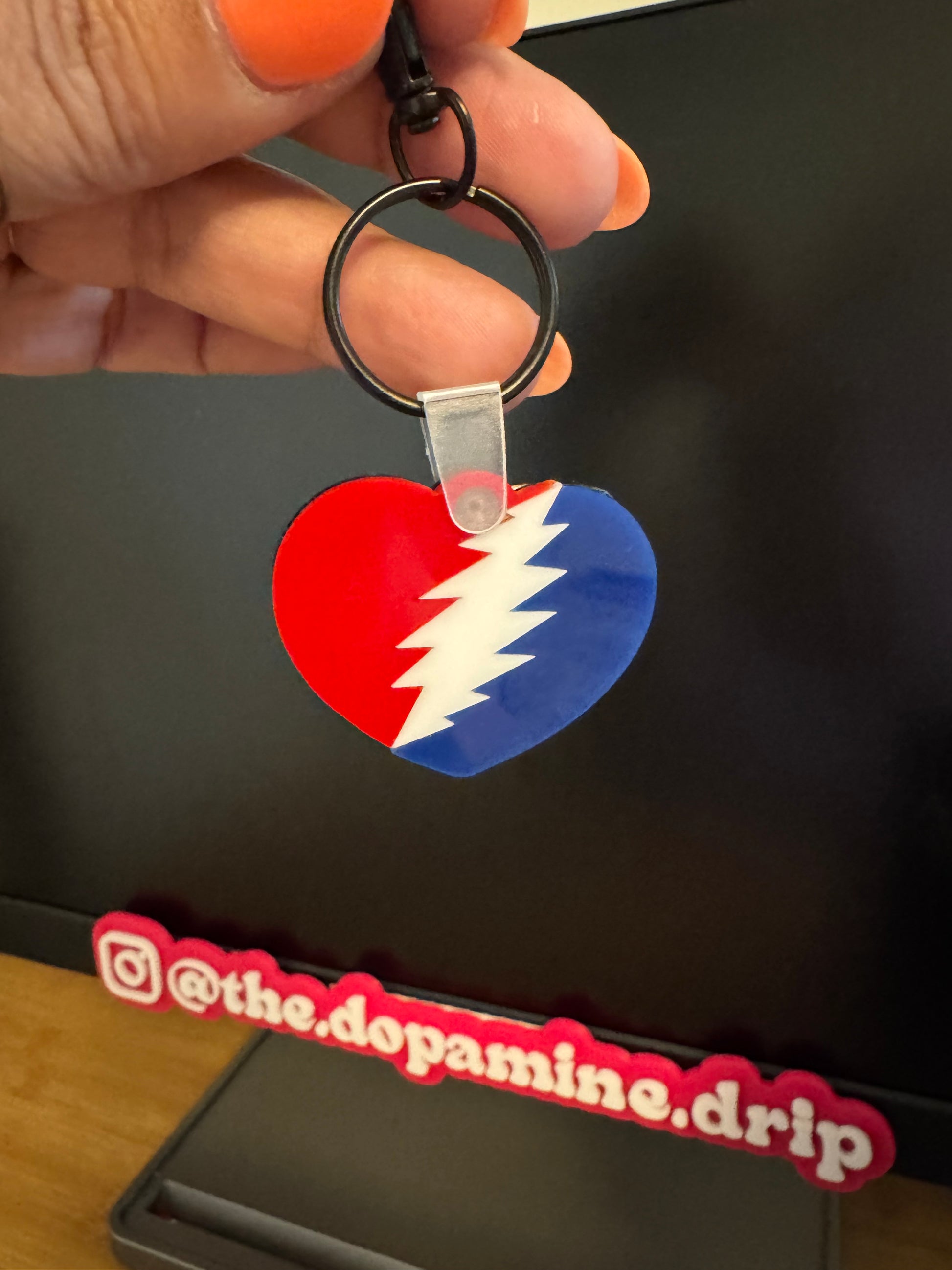 Keychain with a colorful design held by a hand, with a black background and 'the dopamine drip' branding.