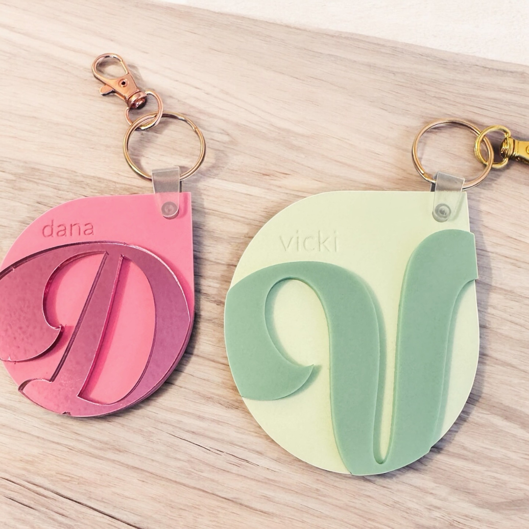 Pink and green keychains with names on a wooden surface